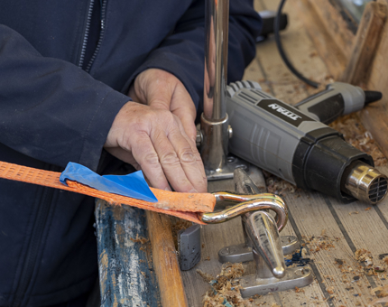 A close up of a hand scraping varnish off of the Royal Barge. There is a heat gun on the side.