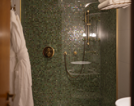 A detailed look at a shower in one of Fingal's cabins. The shower has small green tiles, there is a white robe and towels in the foreground.