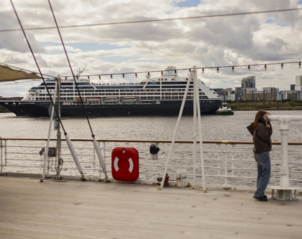 In the Port of Leith in Edinburgh, a cruise ship arrives into the port. A woman is on the deck of Britannia looking through a telescope. 