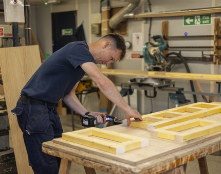 A Maintenance man in the Joiner's Workshop making a frame for shelved in the Shop.