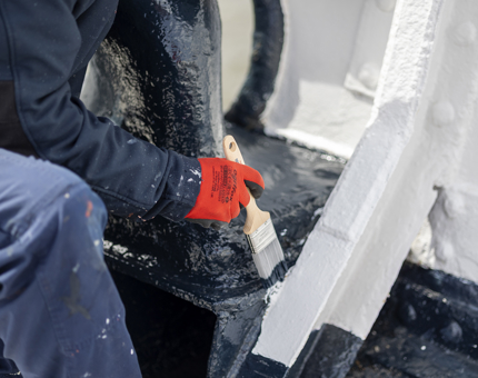 A closer look at a maintenance team member kneeling down to apply a fresh coat of paint to the Fo'c's'le.