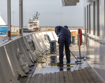 A Facilities Officer is on the deck, he is scrubbing it with a brush.