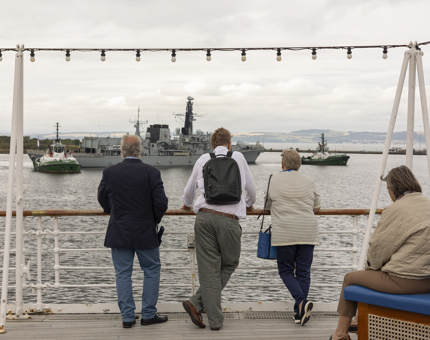 Four people looking into the Port of Leith in Edinburgh where a Navy ship is being towed out. 
