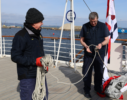Two Maintenance team members on the deck of Britannia preparing the ropes to hoist the set of dress flags.
