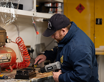 A maintenance man is holding a heat gun to help him remove name plaques from a trophy stand. 