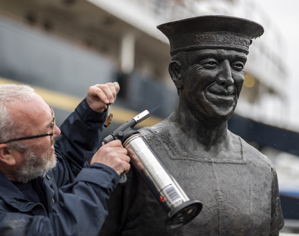 A closer look at a Facilities Officer using a blowtorch to remove oxidisation from a statue of an ex-yachtsman.