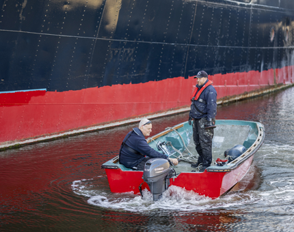 Two men on a small red boat, positioning themselves next to Fingal Hotel.