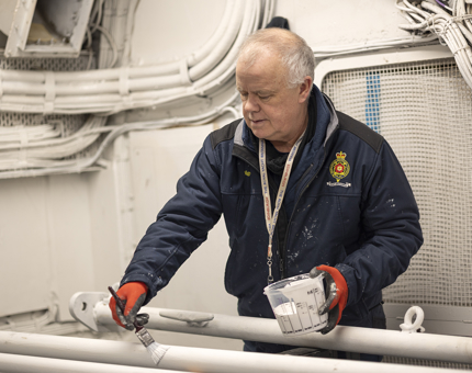 A maintenance team member holding a pot of white paint, painting poles. 