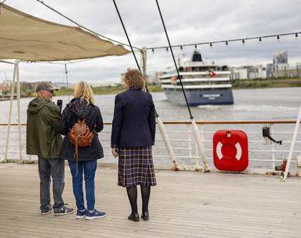 A Visitor Assistant standing on the Verandah Deck with two visitors watching a cruise ship come into the port. 