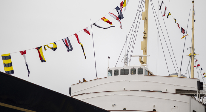 An exterior shot of Britannia, zoomed in on the front of the Bridge area. There are colourful dress flags flying from the mast. 