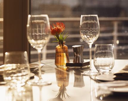 A close up of a table set with glasses and a small vase with an orange flower. 