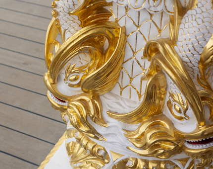 A detailed look at the decorative binnacle. Ornate fish are carved into it and it is painted white and gold. 