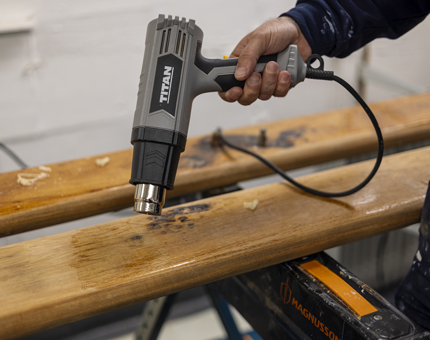 A close look of a hand holding a heat gun to remove varnish from handrails.