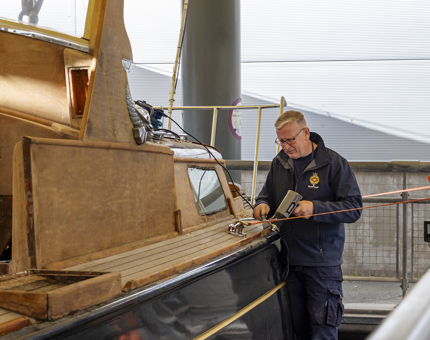 A man holding a heat gun and scraper, removing varnish from the Royal Barge.