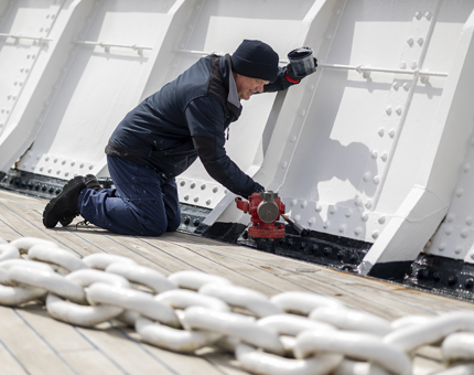A maintenance team member kneeling down to apply a fresh coat of paint to the Fo'c's'le. 