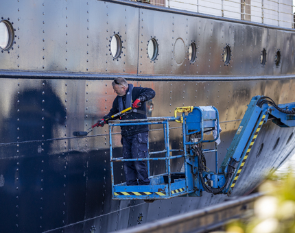 A Maintenance team member applying a coat of blue paint to the side of Fingal.