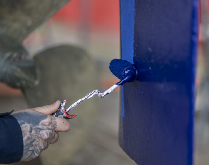 A close up of a hand holding a mini paint roller, painting a boat blue.