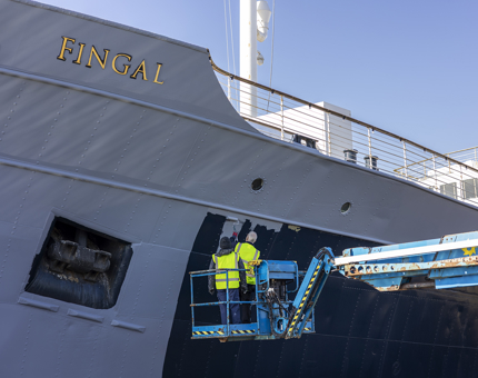 A closer look at two maintenance men painting the side of Fingal. 
