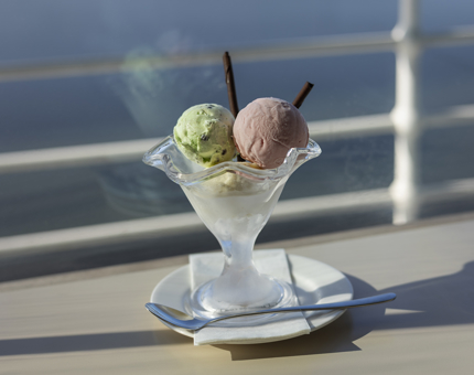 A bowl with 3 scoops of ice cream and chocolate sticks. The sun is shining through the window behind. 