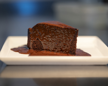 A slice of chocolate fudge cake on a white plate. 