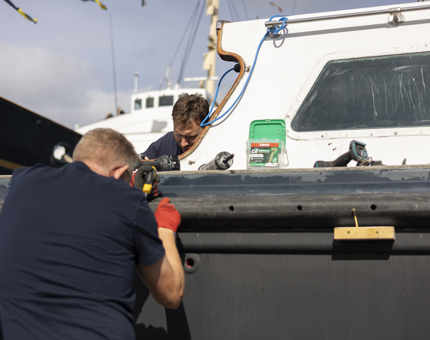 Two Maintenance men are working to refurbish the Admiral's Fast Motor Launch boat.