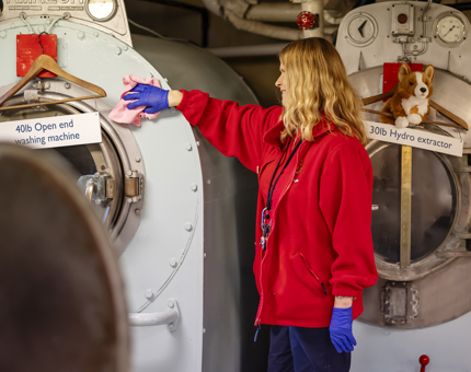 A Housekeeper wearing a red fleece wiping a large washing machine. 