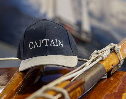 A black and tan coloured baseball cap with the word 'CAPTAIN' on the front of it. 