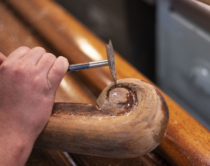 A close up of a hand removing varnish from a decorative end of a handrail. 