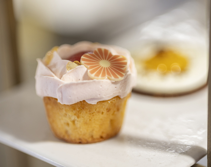 A close up of a cupcake with pink icing and a flower detail. 