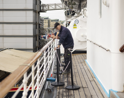 On the port side deck, a maintenance man is cleaning down the decks. 