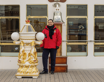 A Visitor Assistant standing by Britannia's Bell and binnacle on the Verandah Deck. 