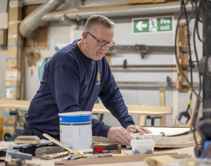 A maintenance team member in the workshop sanding a hatch from a fast motor launch boat.