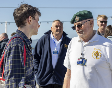 A male visitor chatting with a Yottie who's wearing a white polo short and green beret. There are people in the background. 
