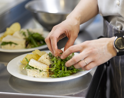 A close up of a chef putting salad on a plate that has a sandwich on it.