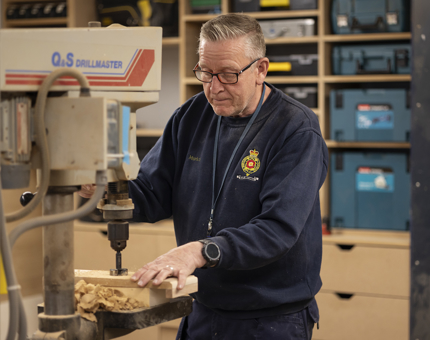A Maintenance team member drilling a hole in some wood.
