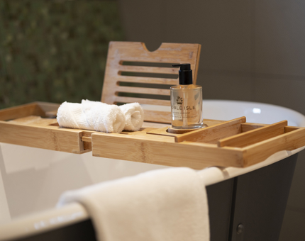 A detailed look at a roll top bath in a cabin aboard Fingal. There is a wooden bath table with white towels and a bottle of Noble Isle bath and body products. 