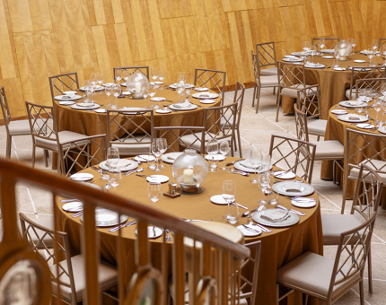 A view from the stairs of tables set for an evening event in the ballroom. the tables have gold coloured table cloths on them.