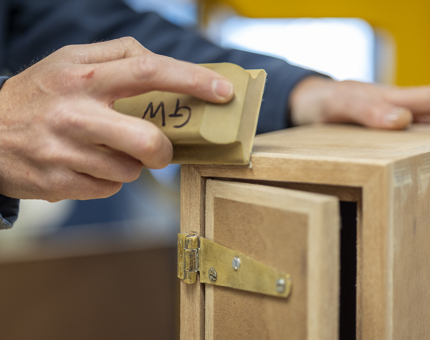 A close-up of a hand holding a sanding block, sanding a wooden box. 