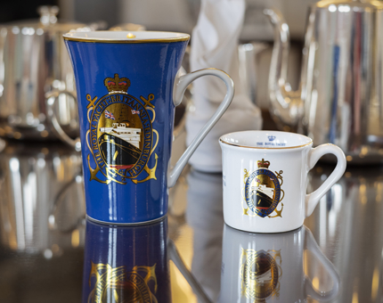 A blue coffee mug and white espresso mug with a Britannia shield on them.
