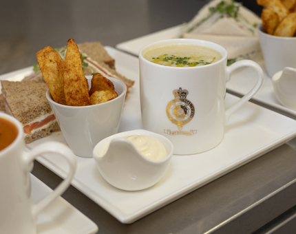 A sandwich, bowl of potato wedges, and mug of soup are on a plate, ready to be served. 