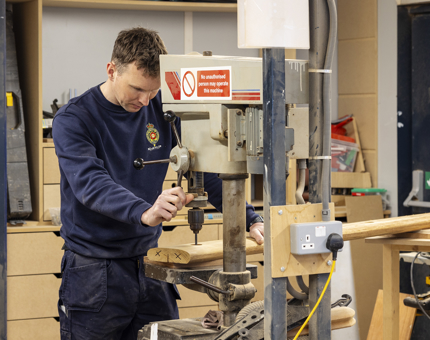 A Maintenance team member drilling a hole in a handrail.