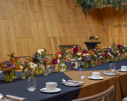 In the Ballroom, there is a long table set for an event. There are vases displayed on the table with autumnal flowers. 