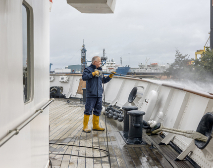 Maintenance team member is holding a power hose, washing down the Poop Deck on Britannia.